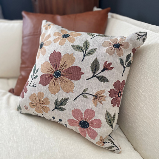 Floral-patterned pillow on a beige couch with a brown leather chair in the background.