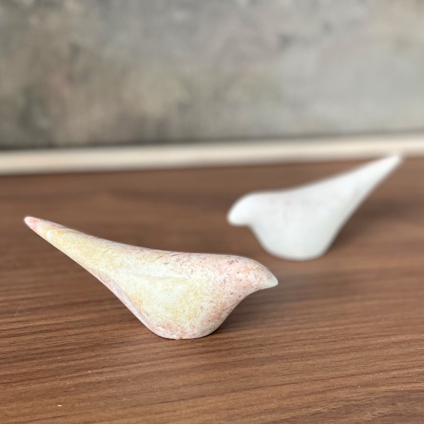 Two stone birds on a wooden surface with a neutral background
