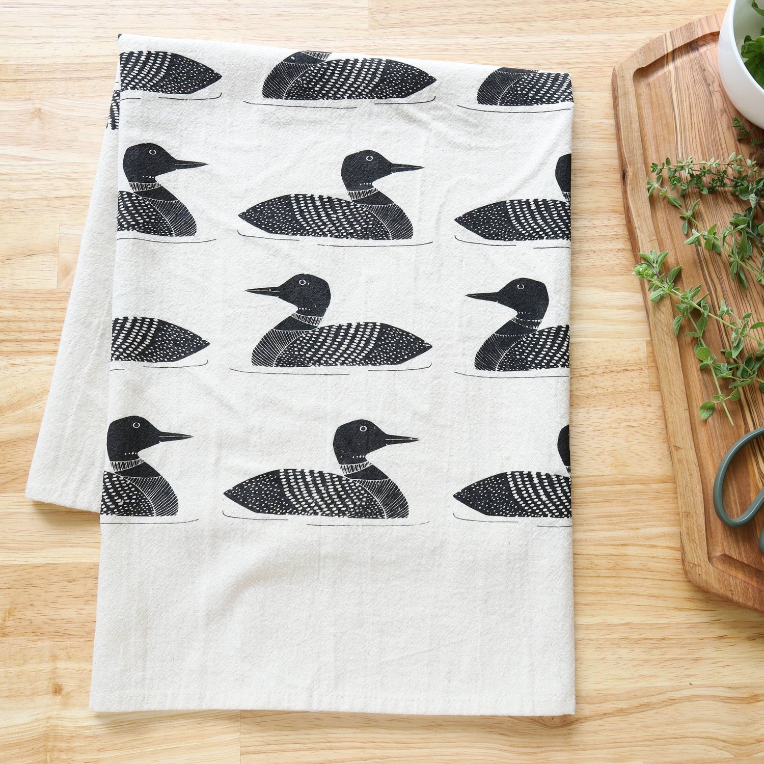 Tea towel with loon pattern on a wooden surface with a cutting board and bowl.