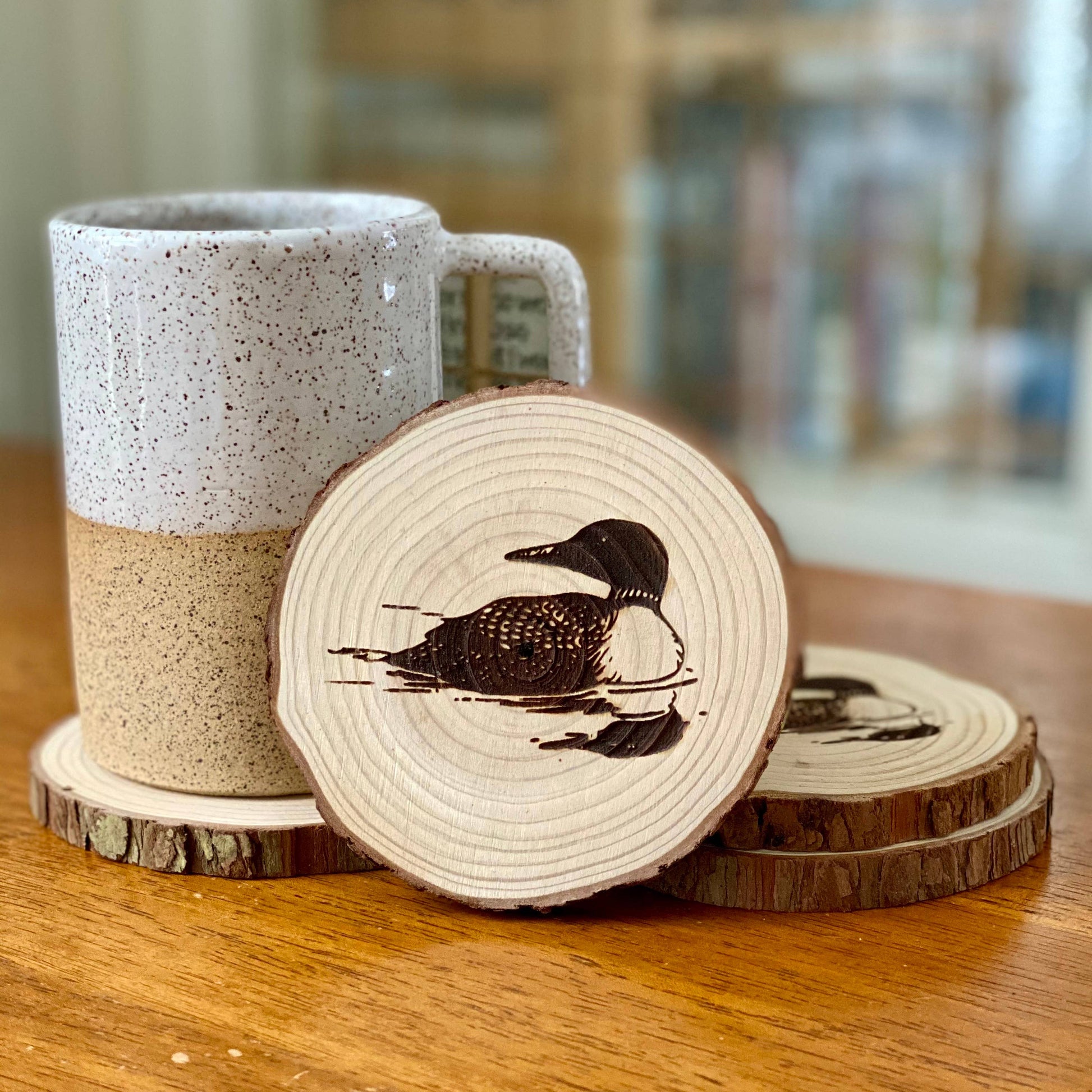 Speckled mug with wooden coasters featuring a loon design on a wooden surface.