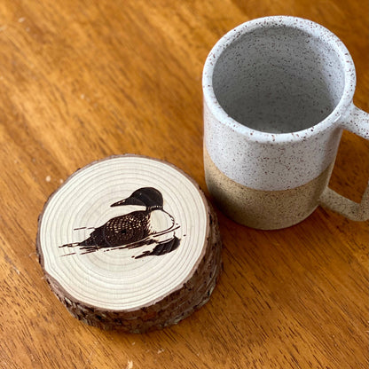 Mug with a wooden coaster featuring a loon design on a wooden surface