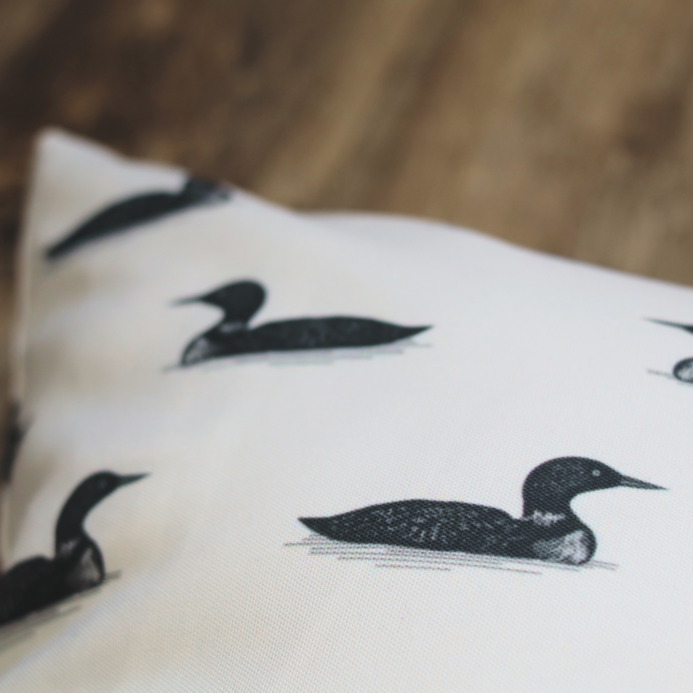 White pillow with black bird illustrations on a wooden surface