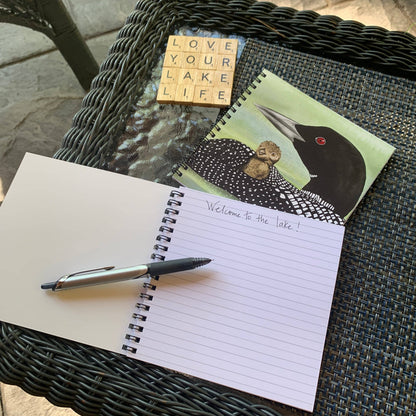 An open lined spiral notebook with a silver pen resting on it, placed on a dark woven patio table. 
