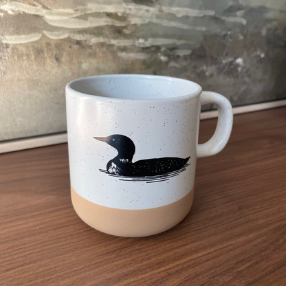 White mug with a black loon illustration on a wooden surface