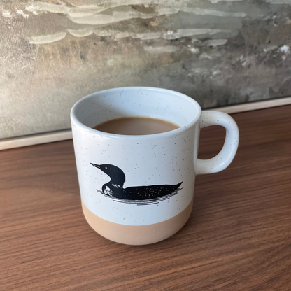 White mug with a black loon design on a wooden surface