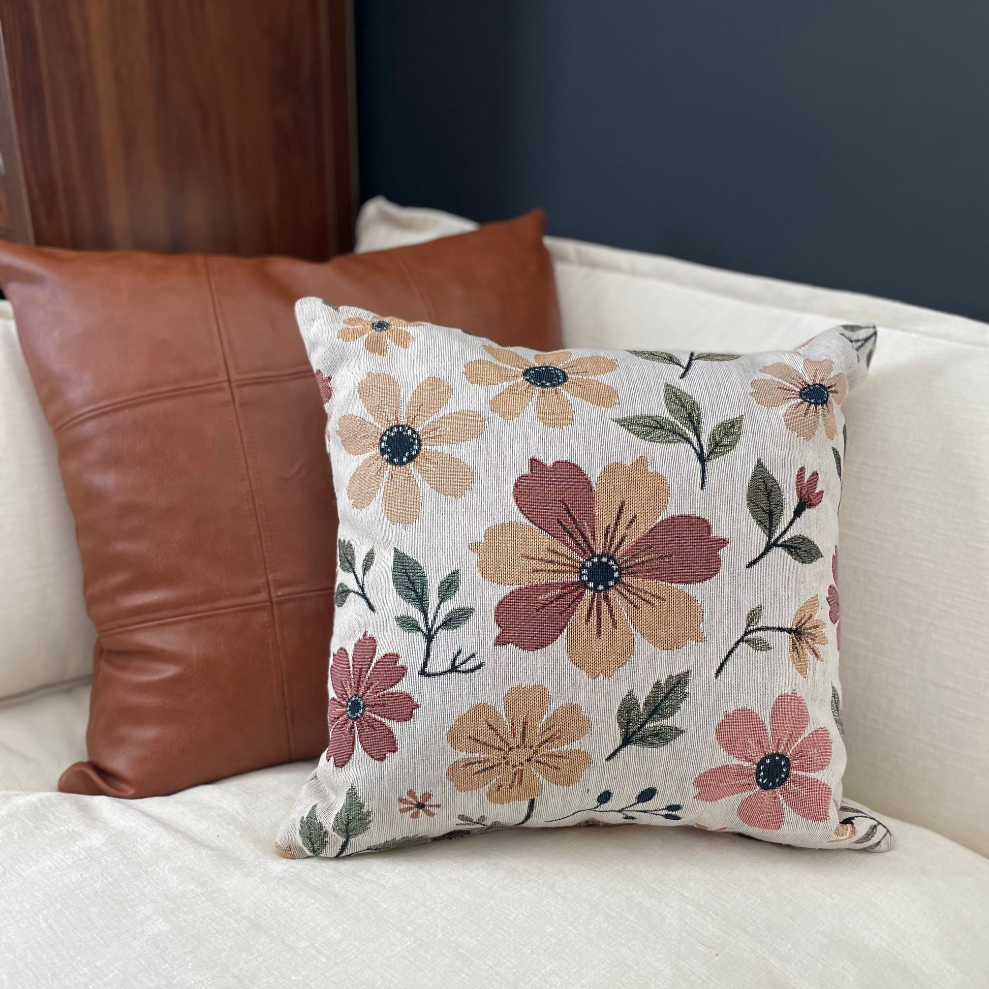 Floral-patterned pillow on a white couch with a brown leather pillow.