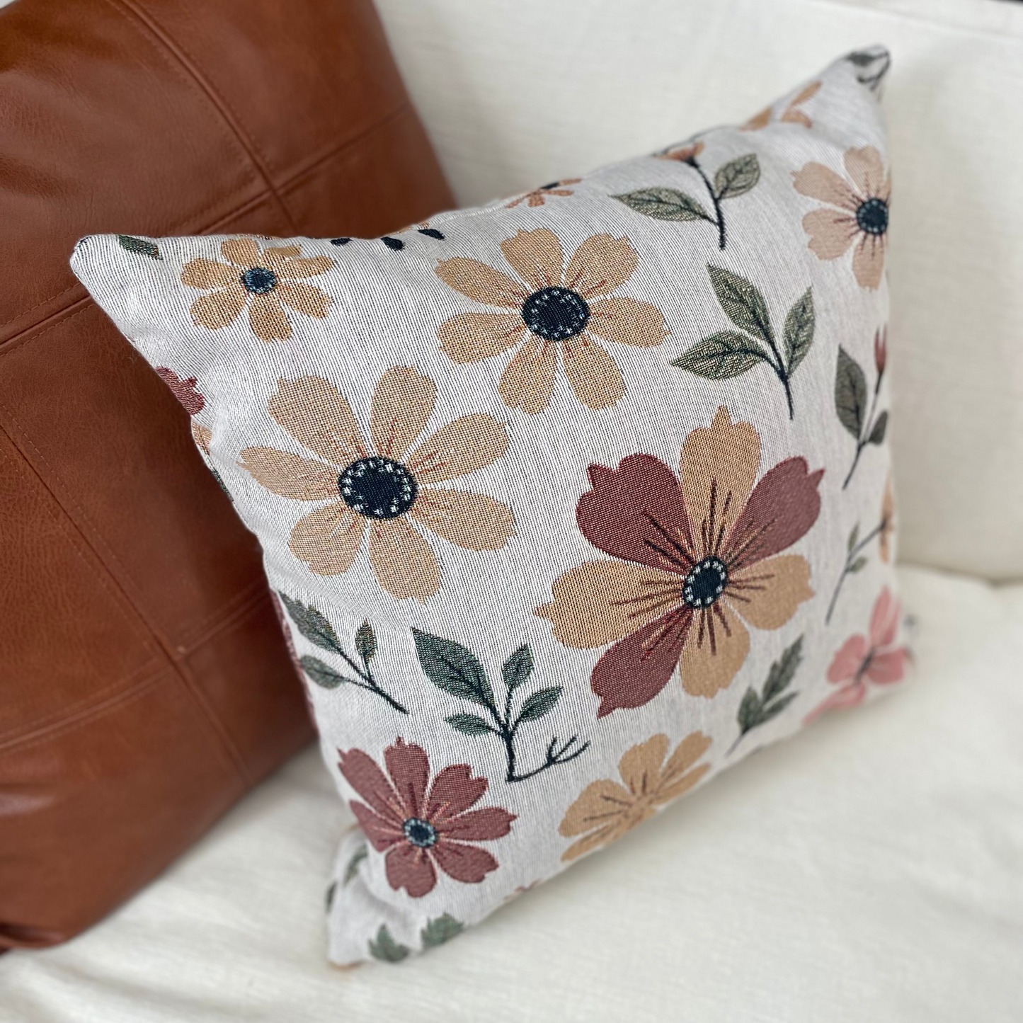 Floral-patterned pillow on a white couch with a brown leather pillow.