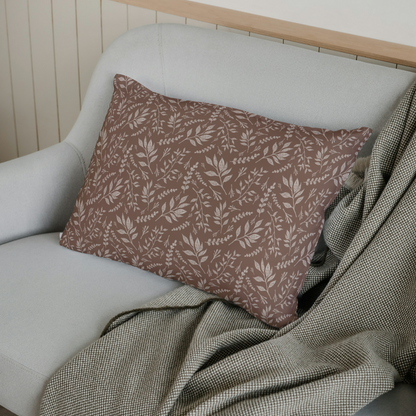 Decorative pillow with leaf pattern on a light gray sofa with a green blanket.