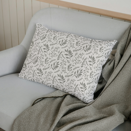 Decorative pillow with leaf pattern on a gray sofa with a green blanket.