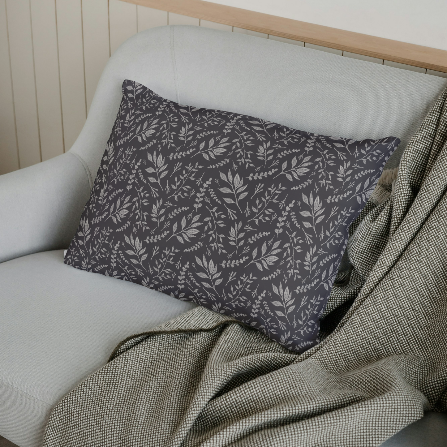 Gray pillow with leaf pattern on a white sofa with a green blanket