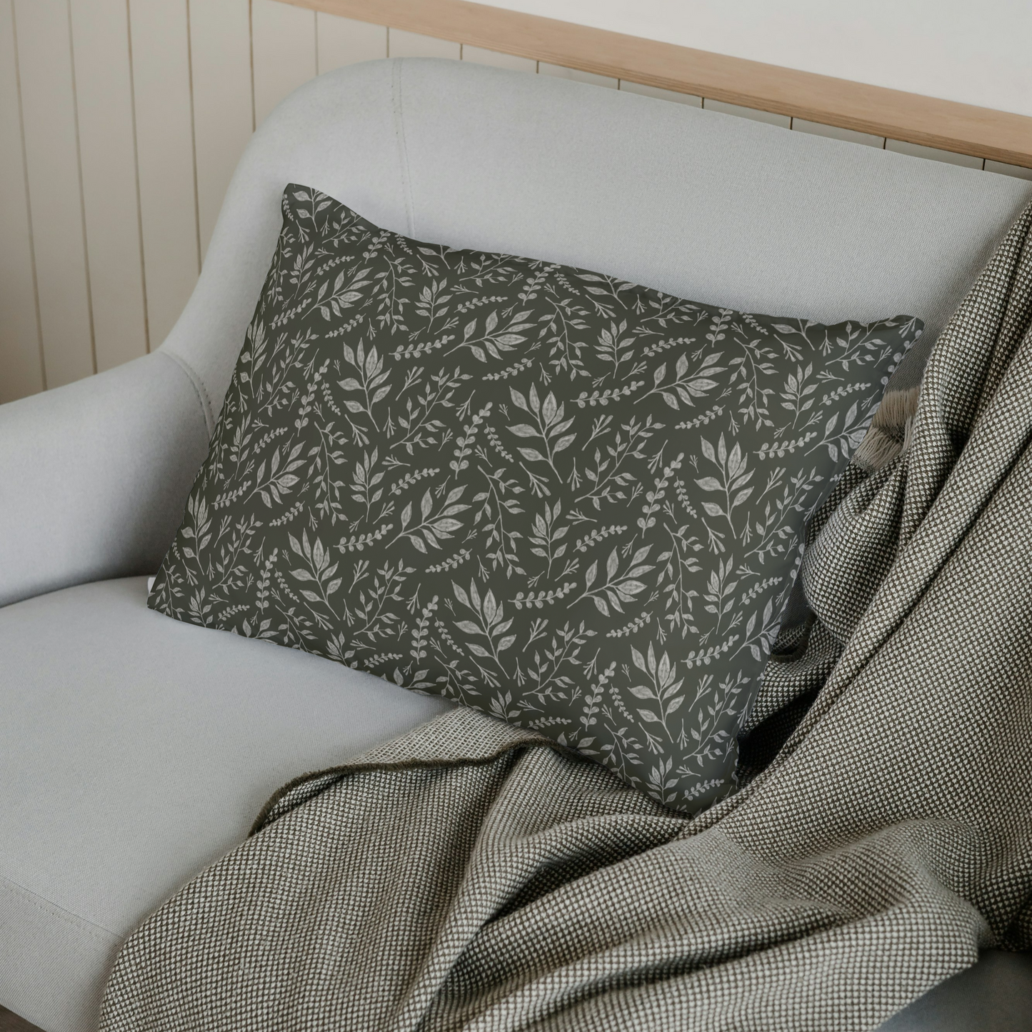 Gray cushion with leaf pattern on a white sofa with a wooden headboard.