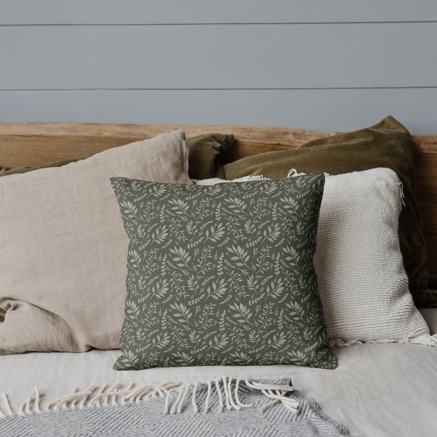 Decorative pillow with a green pattern on a bed with neutral bedding against a gray wall.