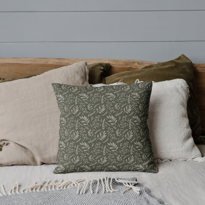 Decorative pillow with a green pattern on a bed with neutral bedding against a gray wall.