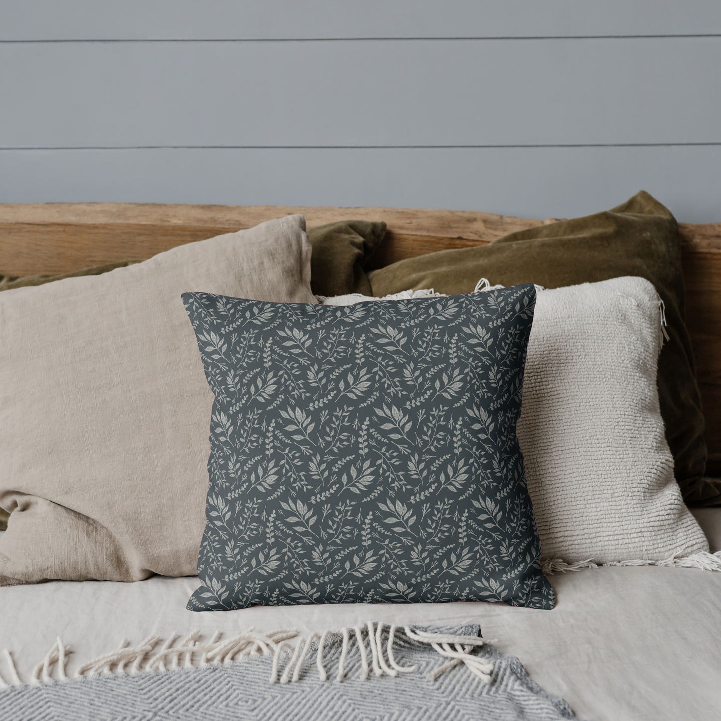 Decorative pillow on a bed with neutral bedding and a gray wall.