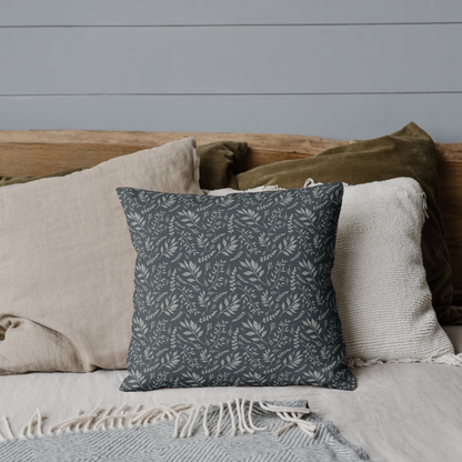 Decorative pillow on a bed with neutral bedding and a gray wall.