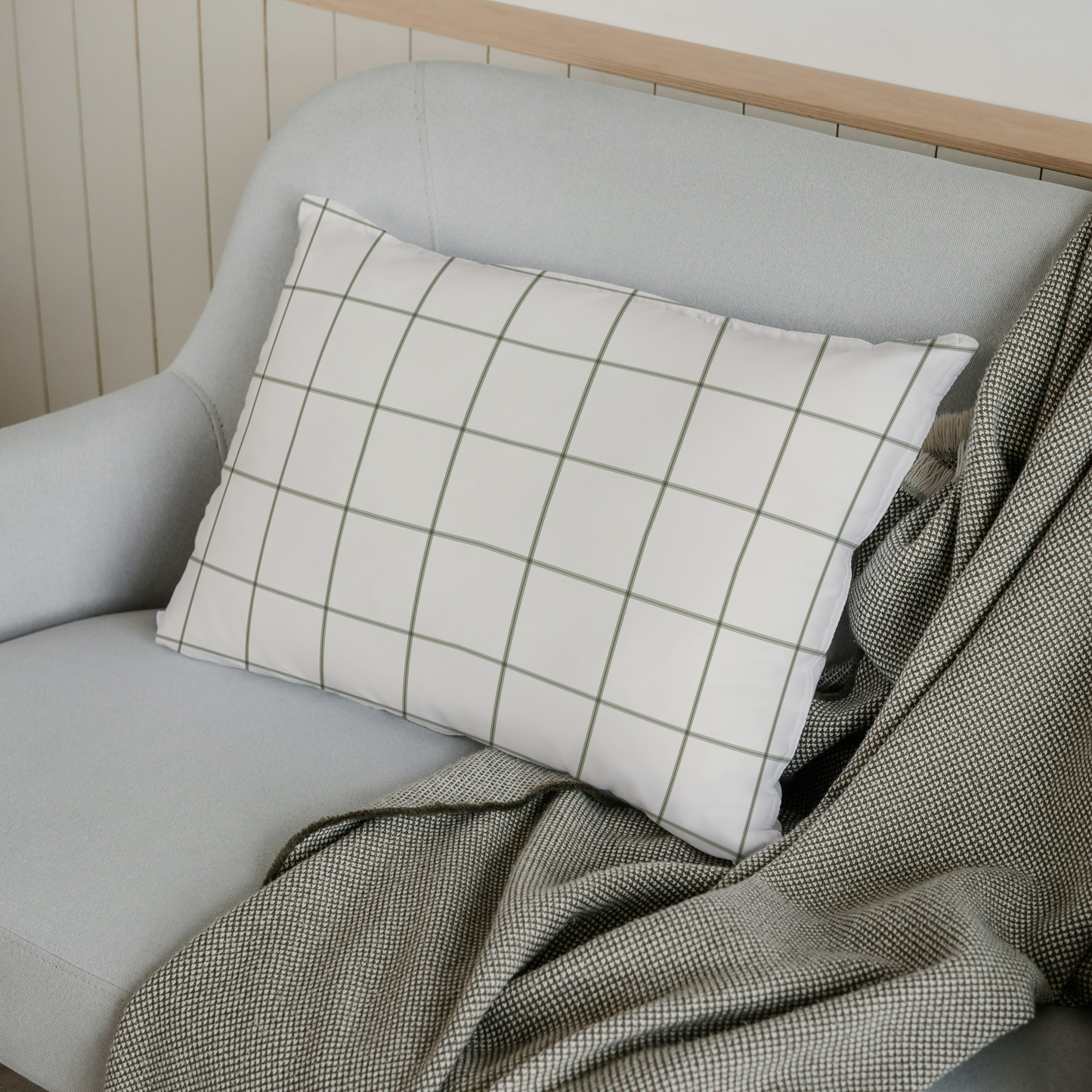 Gray sofa with a plaid pillow and green blanket against a white wall.