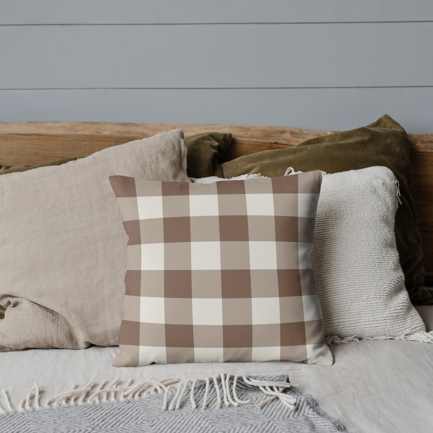 Plaid pillow on a bed with neutral bedding against a gray wall