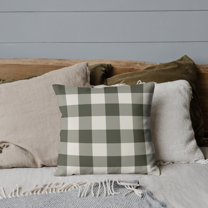 Plaid pillow on a bed with neutral bedding against a gray wall