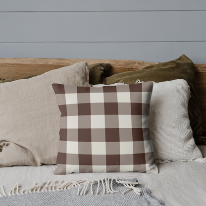 Plaid pillow on a bed with neutral bedding against a gray wall