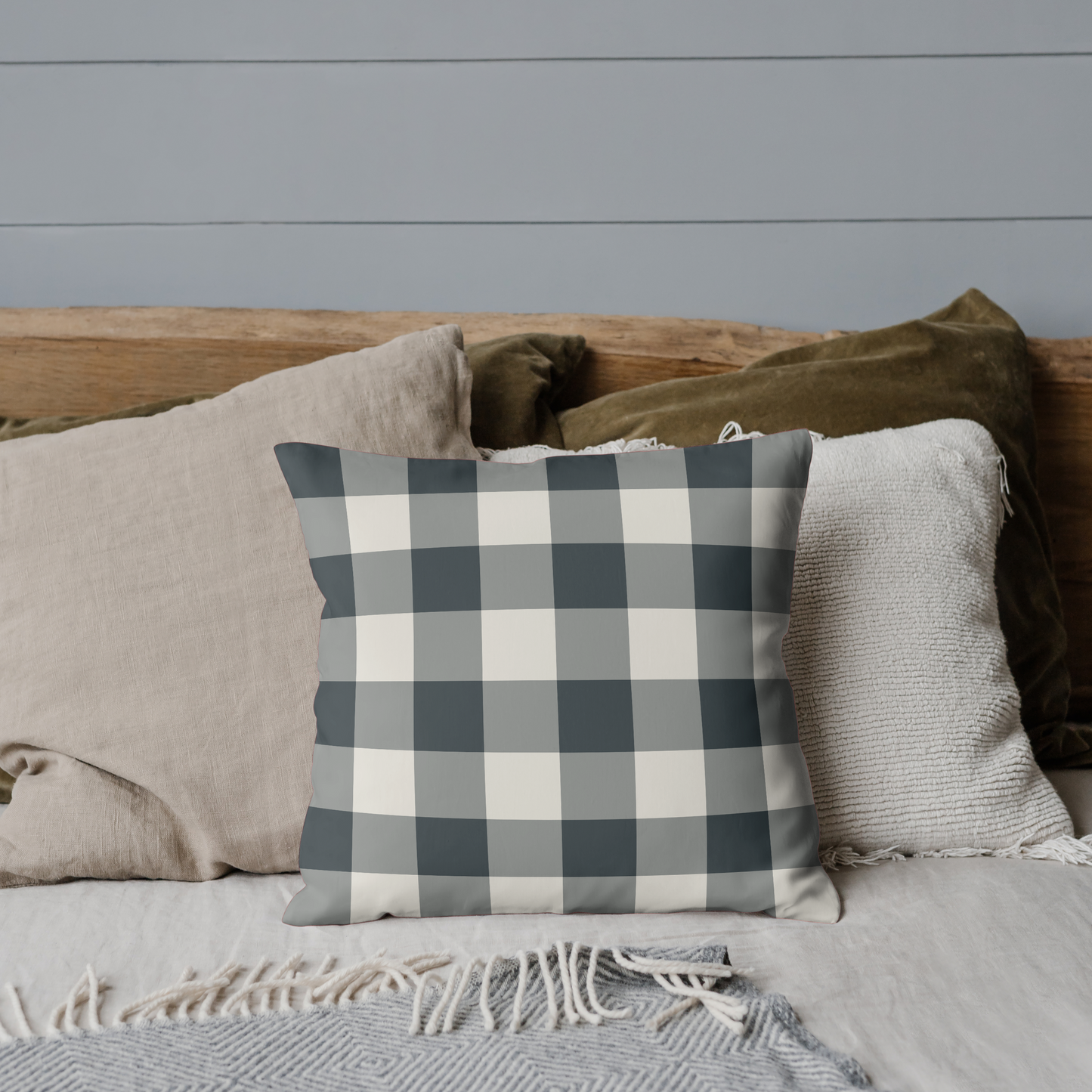 Plaid pillow on a bed with neutral bedding against a gray wall