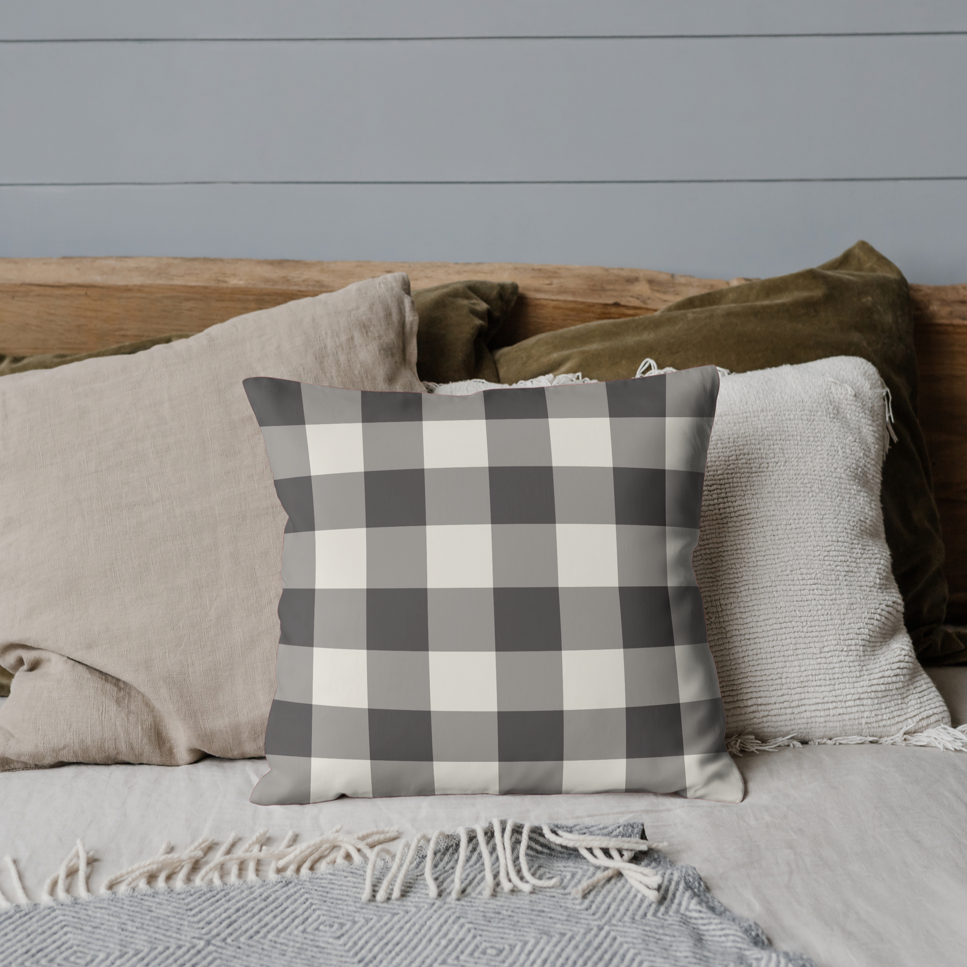 Plaid pillow on a bed with neutral bedding against a gray wall
