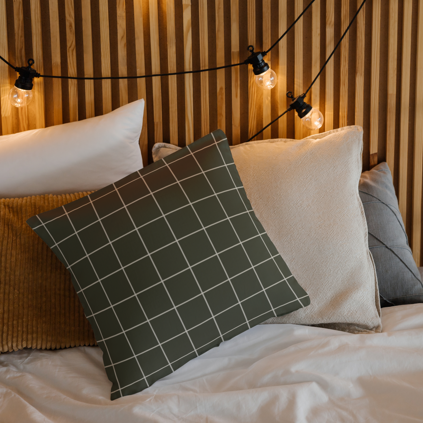 Bed with decorative pillows and string lights against a wooden wall.