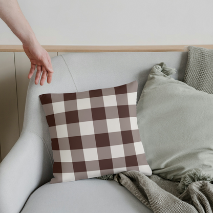 Person adjusting a checkered pillow on a gray sofa with a neutral background
