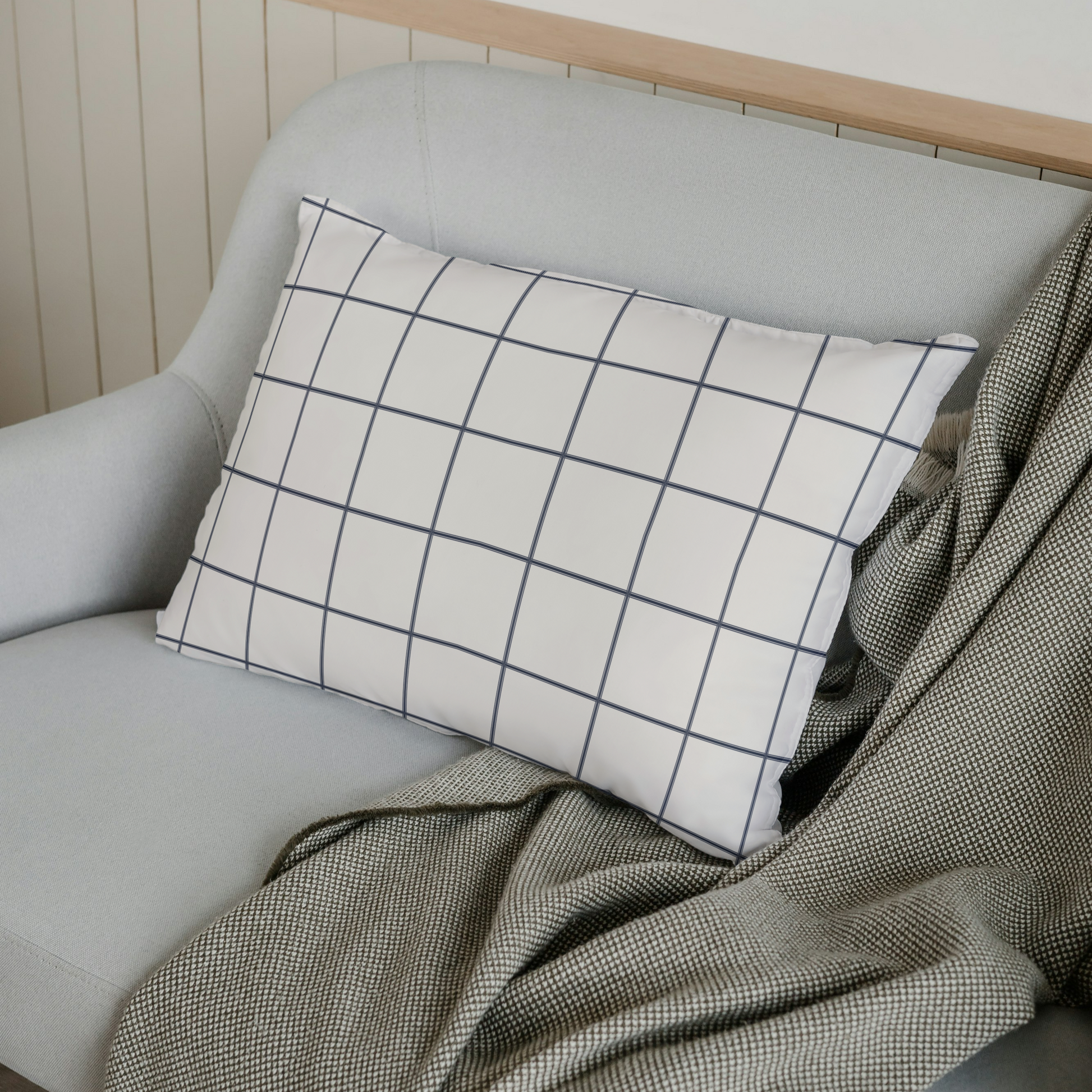 Gray sofa with a grid-patterned pillow and green blanket against a white wall.